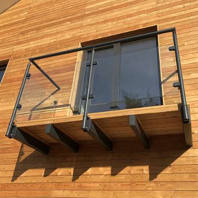 Toto moderní zábradlí na balkoně či terase využívá minimalistickou kombinaci skla, kovu a dřeva, která ladí s celkovým dřevěným obložením fasády.